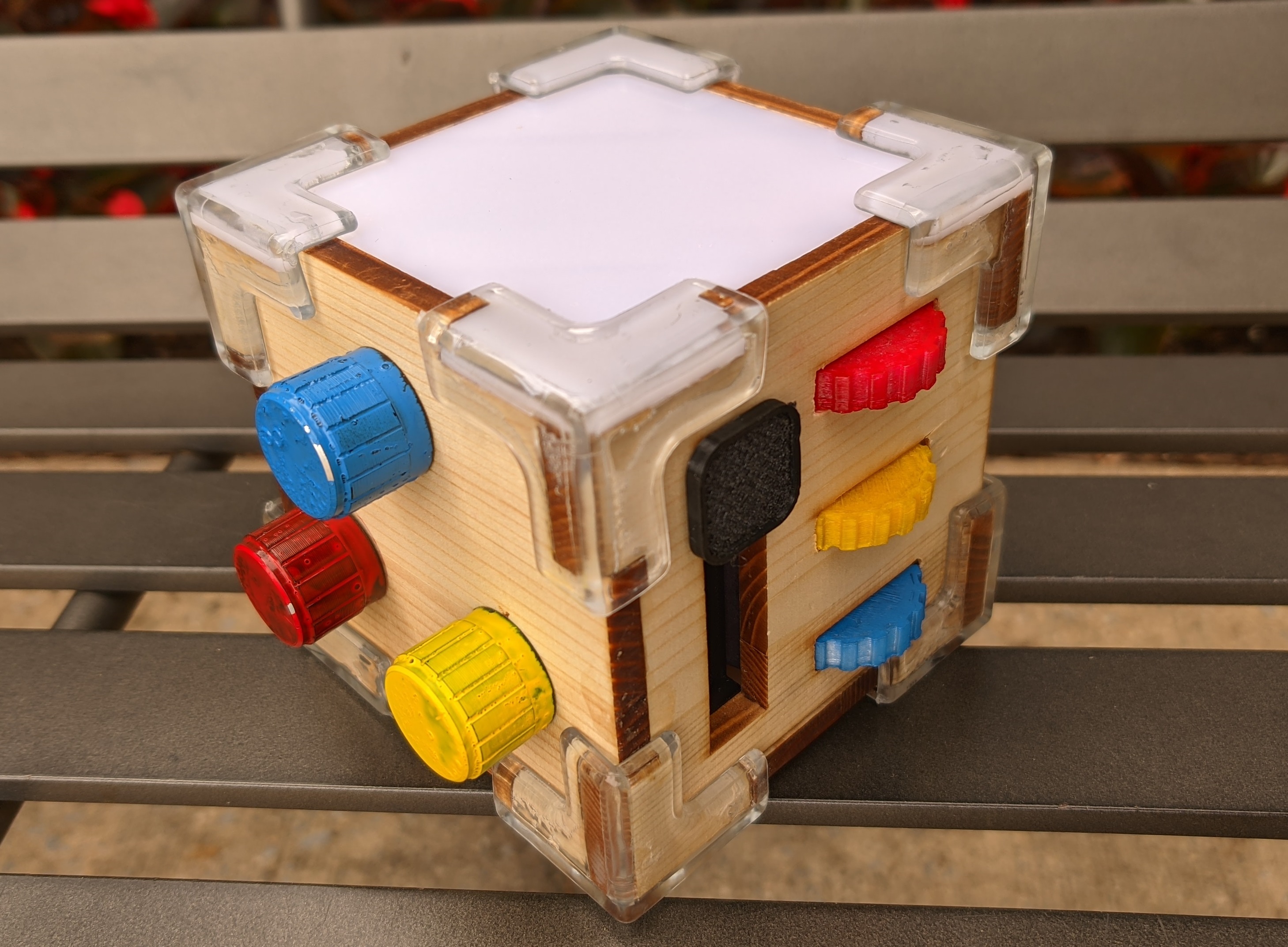 Image of a wooden fidget cube, 
    with 3 buttons on the left side, plexiglass on the top, and balls and switches on the right.